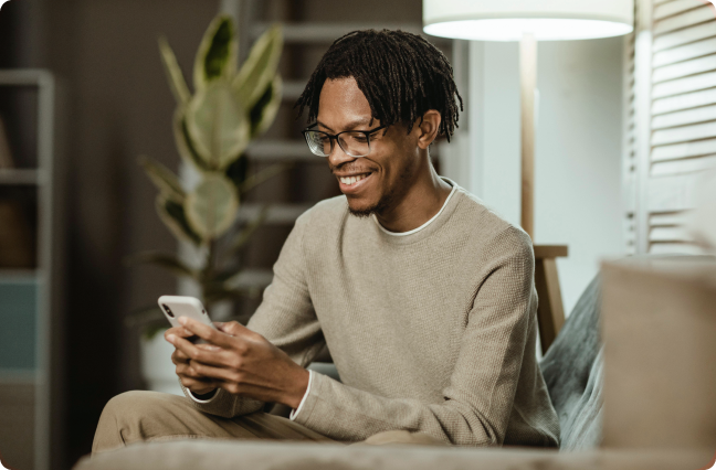 Homem negro com moletom bege mexendo no celular e sorrindo